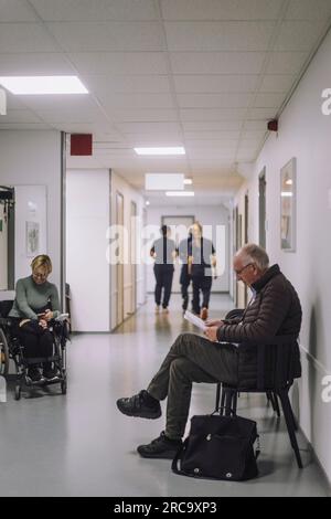 Vue latérale d'un patient âgé assis sur une chaise dans la salle d'attente à l'hôpital Banque D'Images