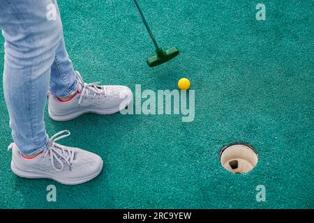 Femme jouant au golf miniature et essayant de mettre la balle dans le trou. Activités de loisirs estivales Banque D'Images