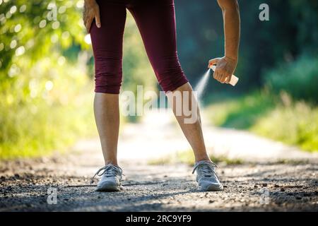 Femme appliquant un insectifuge contre les moustiques et tique sur sa jambe avant de courir dehors Banque D'Images