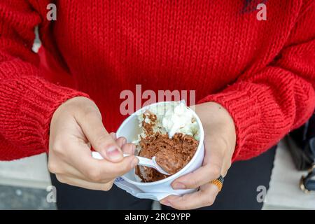 gros plan vue de dessus des mains féminines blanches, tenant une petite tasse de crème glacée à deux saveurs, en prenant une tranche avec une petite cuillère. Banque D'Images