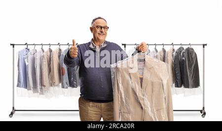 Homme mature recueillant un costume de nettoyeurs à sec et faisant des gestes pouces vers le haut isolé sur un fond blanc Banque D'Images