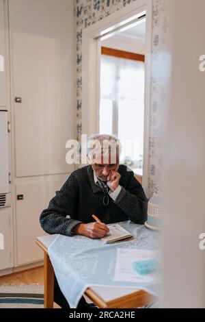 Homme senior avec la main sur le menton résolvant le puzzle Soduko tout en étant assis à la maison Banque D'Images