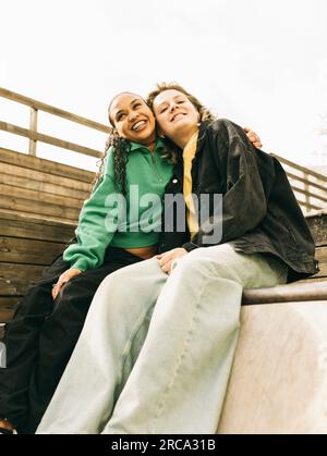 Jeune femme souriante embrassant une amie en étant assise sur des marches Banque D'Images
