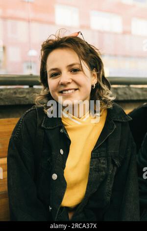 Portrait d'une jeune femme souriante portant une veste en denim assise sur un banc Banque D'Images