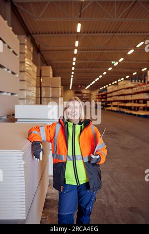 Portrait de cols bleus heureux en vêtements de travail de protection appuyé sur des planches dans l'entrepôt de distribution Banque D'Images
