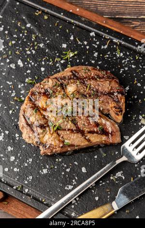 Steak ribeye grillé au romarin et au thym sur une planche à découper en pierre Banque D'Images