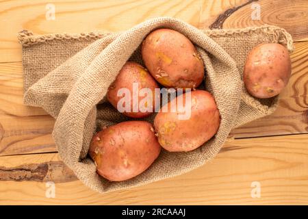 Plusieurs pommes de terre roses crues dans un sac de jute, gros plan, sur une table en bois, vue de dessus. Banque D'Images