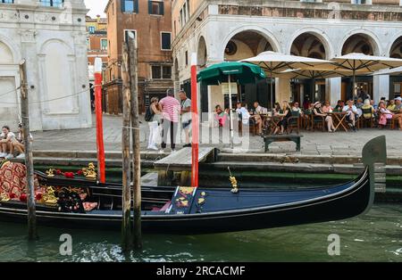 Une gondole amarrée en face de Campo Erbaria sur le Grand Canal avec des touristes à la chaussée cafè en été, Venise, Vénétie, Italie Banque D'Images