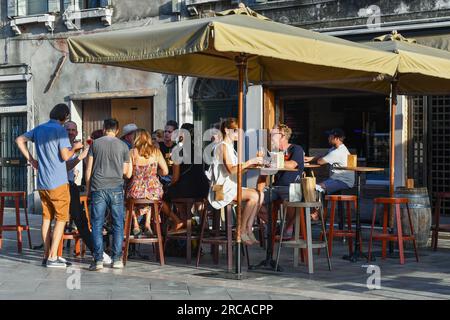 Touristes profitant de leurs apéritifs ('cicchetti') dans une osteria vénitienne typique ('bacaro') dans le sestiere de Castello, Venise, Vénétie, Italie Banque D'Images