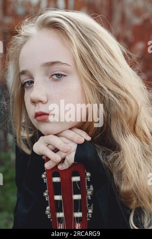 Un adolescent de 13 ans avec une guitare. Musique et hobbies. Une jeune fille musicienne avec de longs cheveux blonds tient pensivement une guitare. Banque D'Images