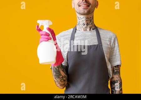 Jeune homme tatoué avec bouteille de détergent sur fond orange, gros plan Banque D'Images