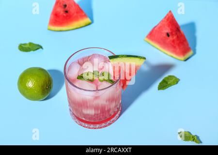 Verre de savoureux cocktail de pastèque avec de la menthe et du citron vert sur fond bleu Banque D'Images