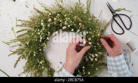 Classe de maître floristique sur le tissage de la couronne de fleurs pour la fête d'Ivan Kupala.Woman tisse la couronne d'herbes fraîches des champs et de fleurs, symbole païen, solstice da Banque D'Images