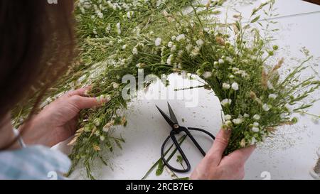 Classe de maître floristique sur le tissage de la couronne de fleurs pour la fête d'Ivan Kupala.Woman tisse la couronne d'herbes fraîches des champs et de fleurs, symbole païen, solstice da Banque D'Images