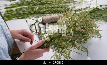 Classe de maître floristique sur le tissage de la couronne de fleurs pour la fête d'Ivan Kupala.Woman tisse la couronne d'herbes fraîches des champs et de fleurs, symbole païen, solstice da Banque D'Images