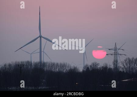 Un soleil d'hiver brumeux se couche derrière des éoliennes près de Grevenbroich, en Allemagne. Banque D'Images