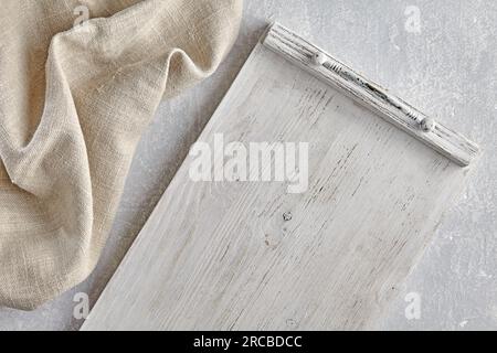 Plateau en bois peint en blanc et serviette de cuisine en lin grossier sur une table en pierre claire. Vue de dessus avec espace de copie. Banque D'Images