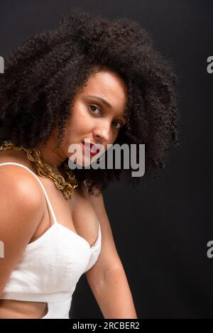 Belle femme, assise, portant des vêtements blancs avec un regard profond vers l'appareil photo. Isolé sur fond gris clair. Banque D'Images