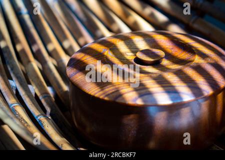 Boîte ronde marron à motifs en bois dans la lumière filtrant à travers les stores Banque D'Images