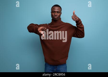 élégant américain de 25 ans, à la peau sombre, avec une coupe courte dans un chandail marron, montre sa main à une idée sur un fond de studio avec un espace de copie Banque D'Images