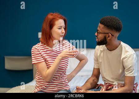 Le jeune couple interracial mari et femme assis sur le lit à la maison discutant des questions d'intimité Banque D'Images