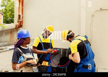 Des techniciens souriants satisfaits des niveaux de fréon dans le climatiseur extérieur tout en utilisant des manomètres à collecteur pour mesurer avec précision la pression du système HVAC, assurant des performances et une efficacité de refroidissement optimales Banque D'Images