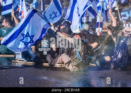 Un manifestant anti-réforme regarde en arrière après avoir été aspergé d'eau bleue par un canon à eau de la police israélienne lors d'une manifestation de réservistes israéliens contre la réforme judiciaire dans laquelle les manifestants ont bloqué l'autoroute tel Aviv - Jérusalem à la jonction Ein Hemed. Banque D'Images