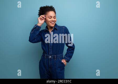 une jeune femme latine brune avec des cheveux afro attachés dans un chignon est habillée dans un costume bleu en denim élégant Banque D'Images