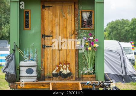 Ford Transit van converti en un mobil-home coloré ou campervan avec des fleurs peintes, des arbres et des poulets lors d'un festival de musique. Banque D'Images