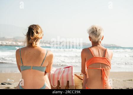 Femmes de l'arrière regardant vers l'horizon sur la plage assis sur le sable. Concept : liberté, détente, déconnexion Banque D'Images