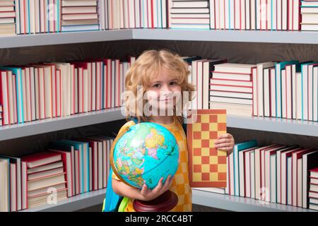 Garçon d'école avec globe du monde et échecs, enfance. École et enfants. Mignon enfant blonde avec un livre d'apprentissage. Journée du savoir. Banque D'Images