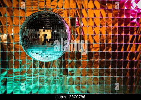 Boule disco brillante contre rideau de fête en aluminium sous la lumière turquoise et orange, espace pour le texte Banque D'Images