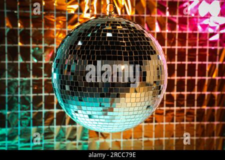 Boule disco brillante contre rideau de fête en aluminium sous la lumière turquoise et orange Banque D'Images