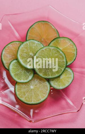 tranches de citron vert vif, roues sur plaque de verre rose, fond rose Banque D'Images