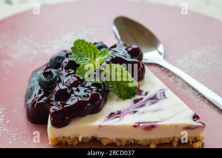Morceau de cheesecake aux myrtilles sur plaque en céramique avec feuilles de menthe poivrée sur le dessus. Banque D'Images
