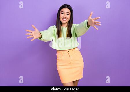 Photo d'adorable fille amicale habillée vert sweat-shirt à bras ouverts prêt vous embrasser isolé fond de couleur violette Banque D'Images