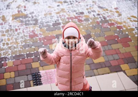 Caucasien souriant heureuse belle petite fille, habillée en veste rose chaude en duvet, souriant à la caméra, debout sur les escaliers dans le porche d'un manoir Banque D'Images