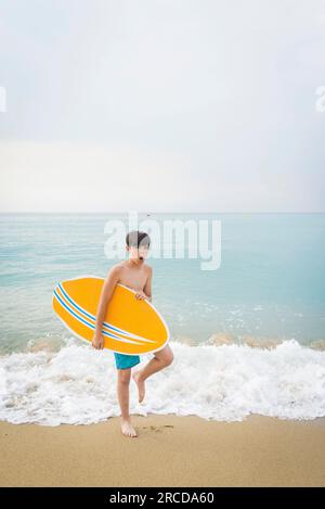 Portrait d'un adolescent souriant joyeux avec planche de surf jaune debout sur la plage Banque D'Images