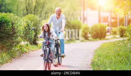 Portraits souriant père avec fille pendant l'été randonnée à vélo en plein air. Ils apprécient la convivialité dans le parc de la ville d'été. Bonne parentalité et chi Banque D'Images