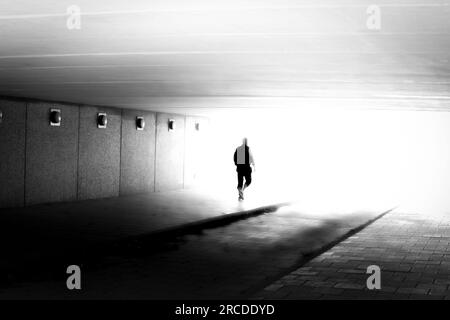 Silhouette méconnaissable d'homme en mouvement floue marchant dans la lumière en noir et blanc Banque D'Images