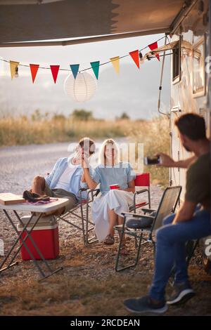 Homme prenant une photo d'un couple. Assis à l'extérieur devant Camper rv. Amusement, convivialité, concept d'amour. Banque D'Images