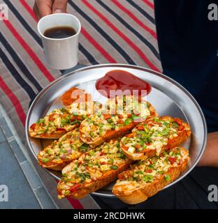 Mains tenant du café noir et du pain à l'ail au gingembre fait maison avec du fromage et des garnitures aux herbes indiennes. Inde Banque D'Images