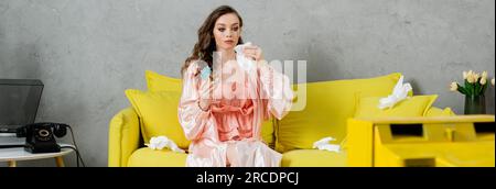 stress émotionnel, femme triste avec du mascara taché assis sur un canapé jaune, femme au foyer avec des yeux pleurant tenant une serviette et un cocktail, regardant la télévision, déprimant Banque D'Images