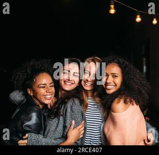 Groupe de quatre amies riantes embrassant la nuit Banque D'Images