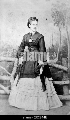 Portrait en pied d'une dame tenant un parasol fermé et vêtue d'une robe de couleur sombre et claire. Photographie originale de John Tredray, artiste et photographe du 3a Robertson Street, Hastings. D'une collection de photographies victoriennes carte de visite, datées des années 1890 Carte de visite est un terme français connu en anglais sous le nom de « Visiting card ». Ils avaient généralement un tirage photographique albumen d'environ 54x89mm monté sur une carte légèrement plus grande. Dans certains cas, les ravages du temps ont fait leurs ravages. Banque D'Images