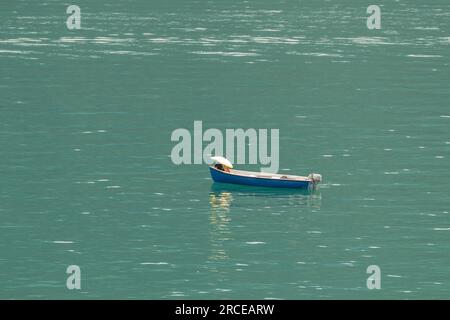Un bateau à moteur bleu sur le lac de Lugano, en Suisse, sur lequel une femme s'abrite du soleil avec un grand parapluie jaune Banque D'Images