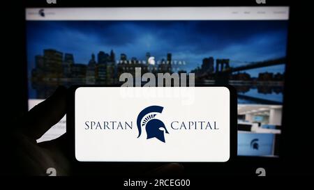 Personne détenant un smartphone avec le logo de la société américaine Spartan Capital Securities LLC sur l'écran devant le site Web. Concentrez-vous sur l'affichage du téléphone. Banque D'Images