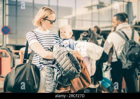 Motherat voyageant avec son bébé garçon enfant. Maman tenant un sac de voyage et son bébé garçon enfant tout en faisant la queue pour le bus devant l'aéroport ter Banque D'Images