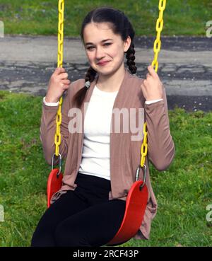 Un jeune adolescent est assis sur une balançoire rouge. Elle a des tresses et est grinçant à la caméra. Les chaînes sur la tourelle sont jaunes. Banque D'Images