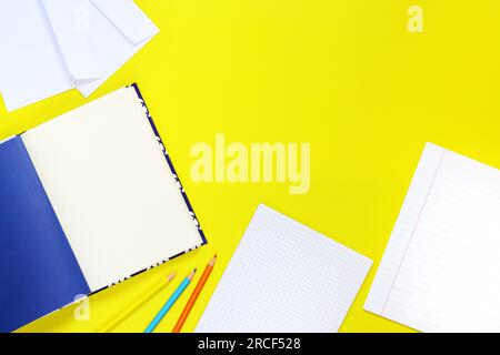 Retour à l'école. Espace de travail, vue de dessus, mise à plat. Ouvrez les cahiers, crayons et enveloppes sur un fond jaune. Des cahiers de notes et un ensemble de papeterie Banque D'Images